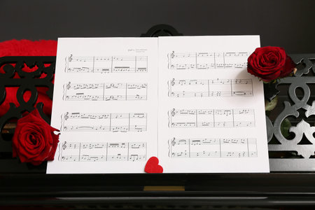 Note sheets with roses for Valentine's Day on piano against dark background, closeupの写真素材