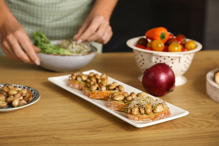 Tasty vegan bruschettas on table against woman cooking in kitchen, closeupの写真素材