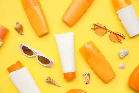 Composition with bottles of sunscreen cream, seashells and sunglasses on yellow background