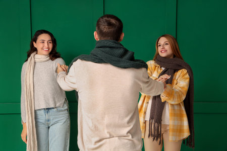 Man and two beautiful women in autumn clothes holding hands on green background. Polyamory concept