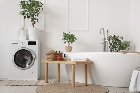 Interior of light bathroom with bathtub, houseplants and wooden benchの写真素材