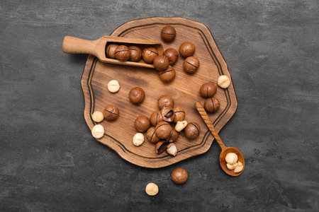 Wooden scoop and board with tasty macadamia nuts on black backgroundの写真素材