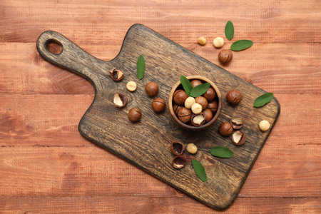 Bowl and board with tasty macadamia nuts on wooden backgroundの写真素材