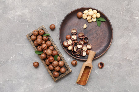 Wooden tray and plate with tasty macadamia nuts on gray backgroundの写真素材