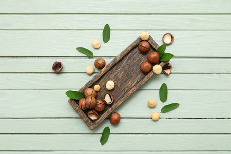 Tray with tasty macadamia nuts and leaves on green wooden backgroundの写真素材