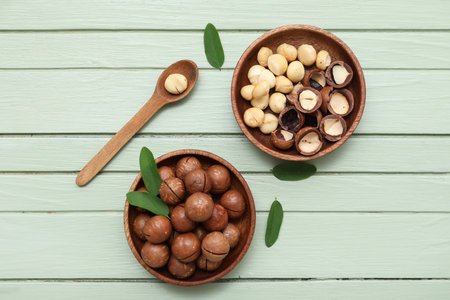 Bowls and spoon with tasty macadamia nuts on green wooden backgroundの写真素材