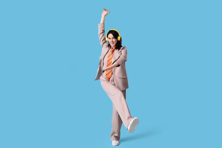 Happy young woman in suit with headphones dancing on blue backgroundの写真素材