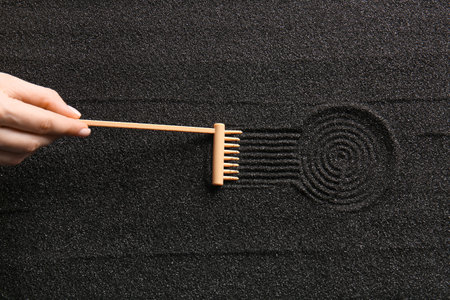 Female hand and small rake on black sand with lines. Zen conceptの写真素材