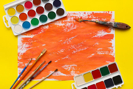 Artist brushes, paints and abstract orange painting on yellow backgroundの写真素材