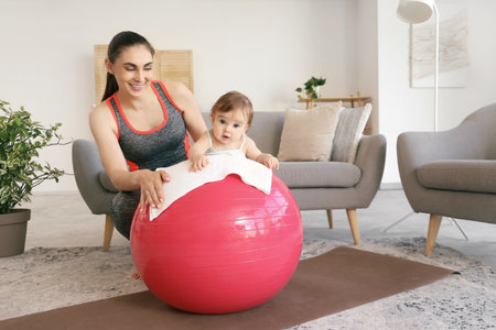 Sporty mother with her little baby on fitball at homeの写真素材