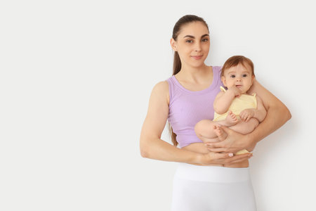 Sporty young mother with her little baby on light backgroundの写真素材
