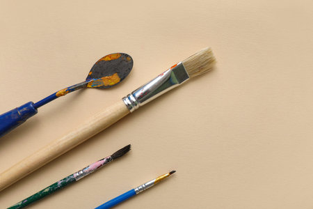 Artist brushes and palette knife on beige background, closeup