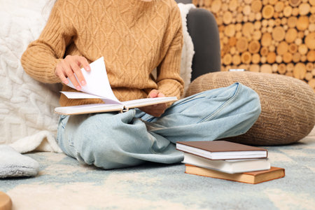 Beautiful young woman reading book on floor at home, closeup