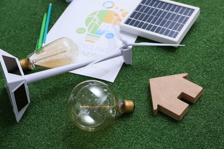 Wind turbine with light bulb and house figure on grass, closeup. Green Energy concept