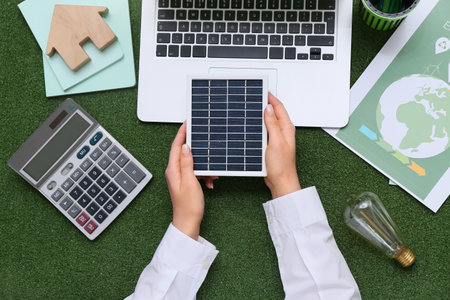Woman with solar panel, laptop, calculator and light bulb on grass. Green Energy conceptの写真素材