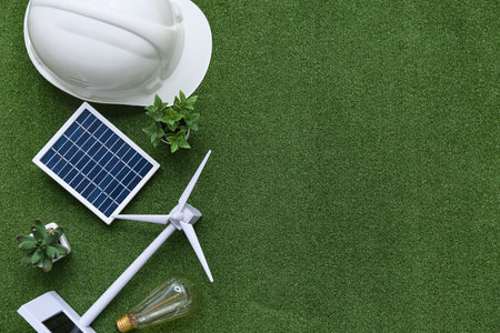 Wind turbine with solar panel, plants, hardhat and light bulb on grass. Green Energy conceptの写真素材