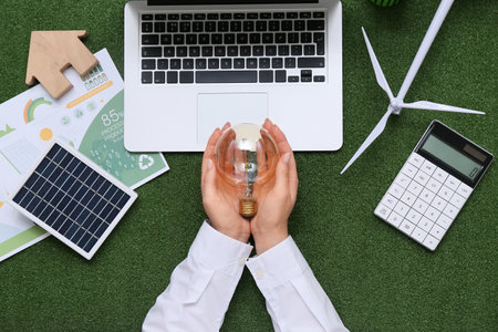 Woman with light bulb, solar panel, laptop and wind turbine on grass. Green Energy conceptの写真素材