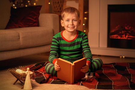 Little boy reading Christmas story on plaid at home in eveningの写真素材