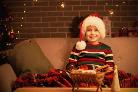 Little boy with Santa hat reading Christmas story on sofa at home in eveningの写真素材