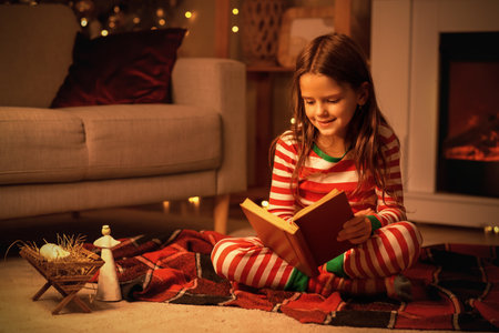 Little girl reading Christmas story on plaid at home in eveningの写真素材