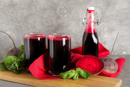 Glasses and bottle of fresh beet juice with basil on gray background