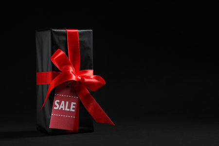 Gift box with red ribbon and label on dark background. Black Friday saleの写真素材