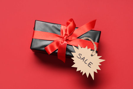 Gift box with ribbon and label on red background. Black Friday sale. Top viewの写真素材