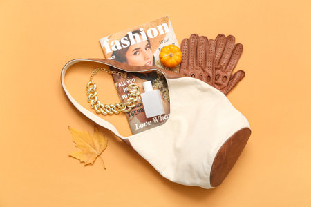 Stylish female bag with leather gloves, magazine and accessories on orange background