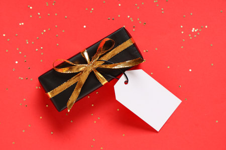 Black gift box and confetti on red backgroundの写真素材