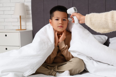 Mother measuring her ill little son's temperature in bedroomの写真素材