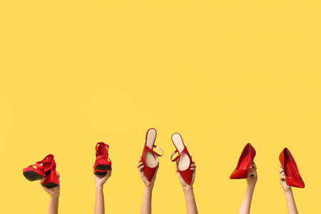 Female hands with stylish red high heeled shoes on yellow backgroundの写真素材