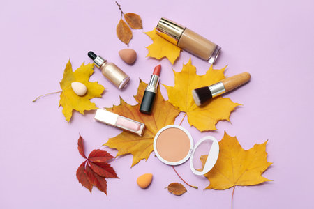 Composition with decorative cosmetics, makeup accessories and autumn leaves on lilac backgroundの写真素材