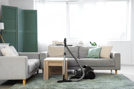Interior of light living room with vacuum cleaner, sofas and tableの写真素材