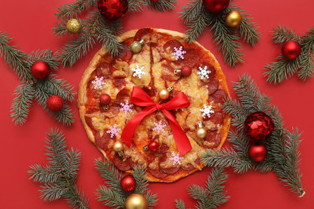 Composition with delicious pizza slices, fir branches and Christmas decor on red backgroundの写真素材