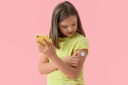 Diabetic girl with glucose sensor using mobile phone for measuring blood sugar level on pink backgroundの写真素材