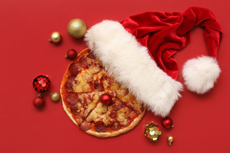Composition with delicious pizza, Santa hat and Christmas balls on red backgroundの写真素材