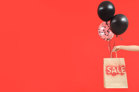 Woman holding shopping bag with balloons on red background. Black Friday Saleの写真素材