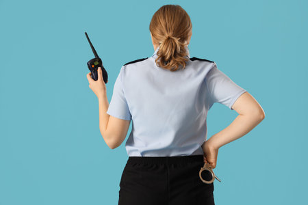 Young female police officer with radio transmitter and handcuffs on blue background, back view. Woman in male profession conceptの写真素材