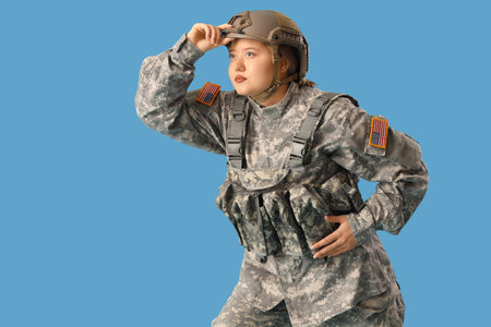 Vigilant young female soldier on blue background. Woman in male profession conceptの写真素材