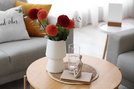Vase with beautiful dahlia flowers, glass of water and book on coffee table in living roomの写真素材