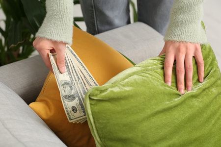 Woman hiding dollar banknotes under cushion on sofa at home, closeupの写真素材