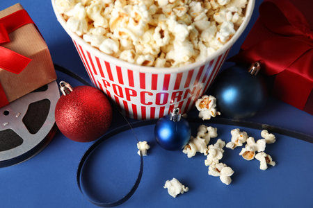 Bucket of popcorn, film reel, gift boxes and Christmas balls on blue background, closeupの写真素材