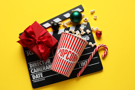 Bucket of popcorn, movie clapper, gift box and Christmas decor on yellow backgroundの写真素材