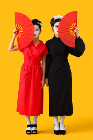 Beautiful young geishas with fans on yellow backgroundの写真素材