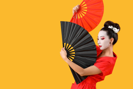 Beautiful young geisha with fans on yellow backgroundの写真素材