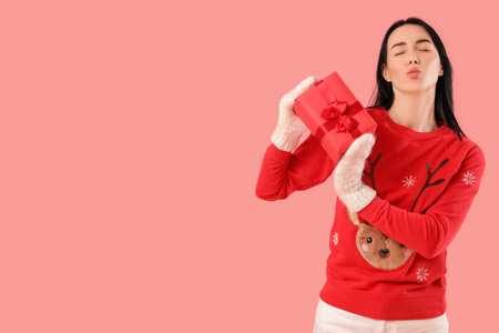 Pretty young woman with Christmas gift box blowing kiss on pink backgroundの写真素材