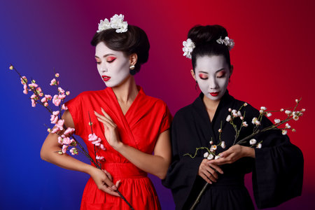 Beautiful young geishas with sakura branches on color backgroundの写真素材