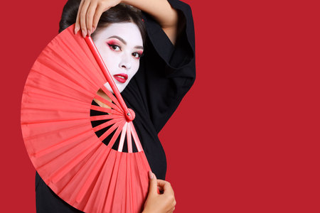 Beautiful young geisha with fan on red backgroundの写真素材