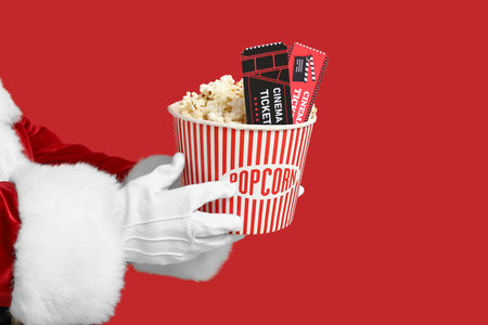 Santa's hands with bucket of popcorn and cinema tickets on red backgroundの写真素材