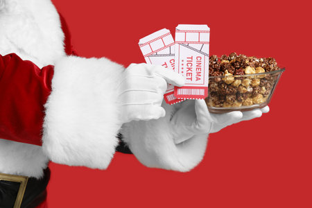 Santa's hands with bowl of sweet popcorn and cinema tickets on red backgroundの写真素材